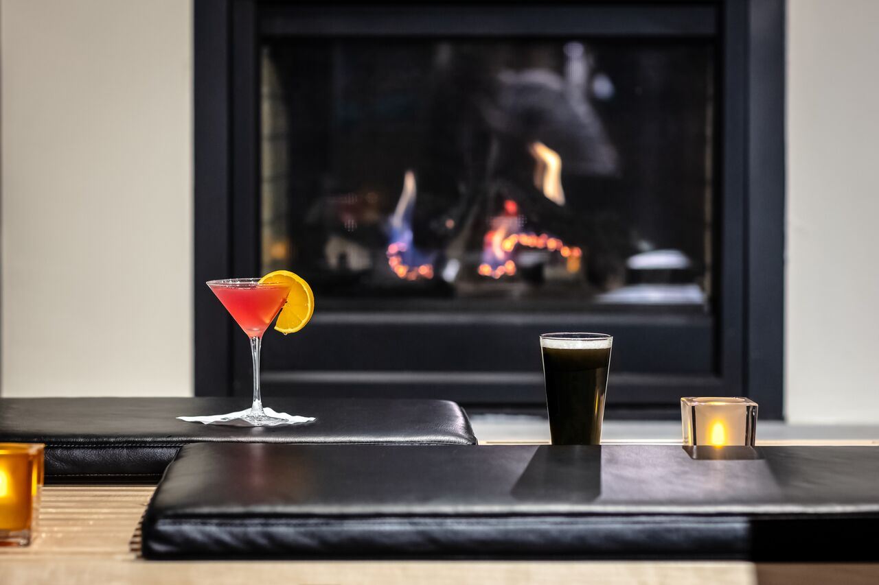 Martini Glass With Red Drink and Pint Glass With Dark Beer In Front of Fireplace