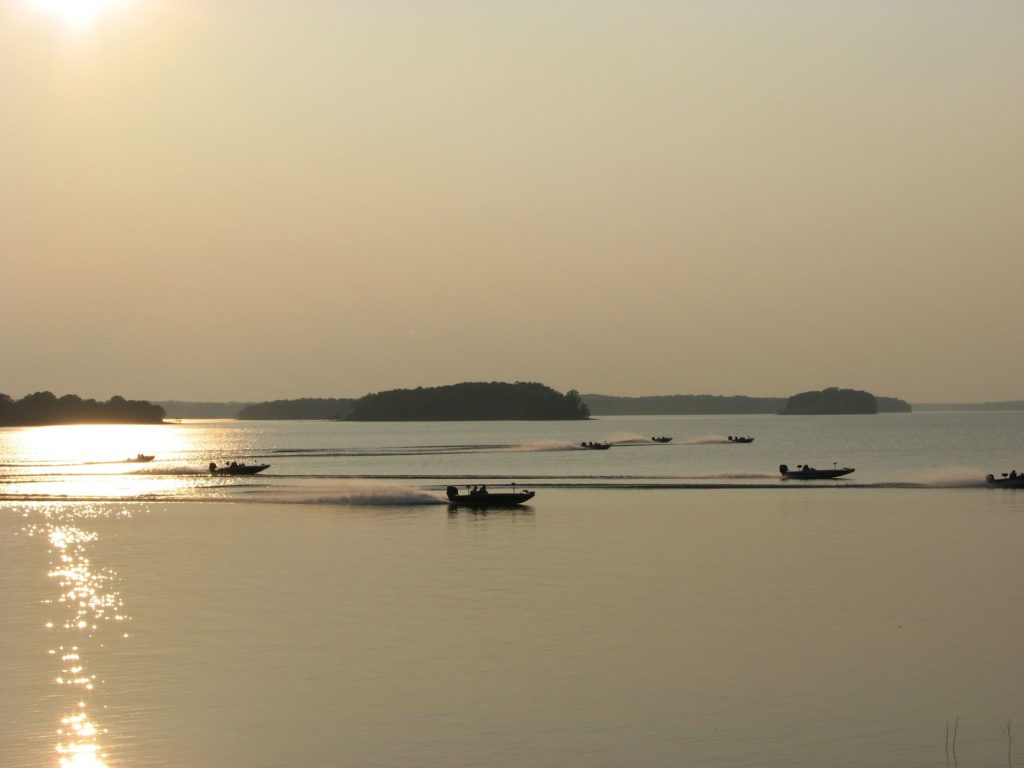 Eight fishing boats gliding across flat lake at sunrise