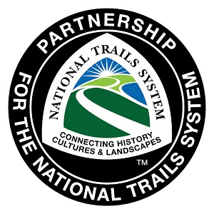Circle logo with outer rim saying partnership for the national trails system. inside the circle in the shape of a tent/triangle with a greenway trail leading to a sunset graphic. text: national trails system connecting history cultures and landscapes