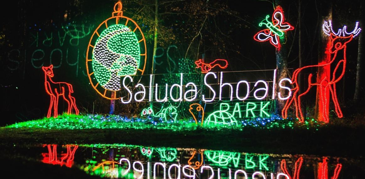 holiday lights on the river at saluda shoals lit up christmas yard art depicting the name saluda shoals park with animals and the saluda shoals logo