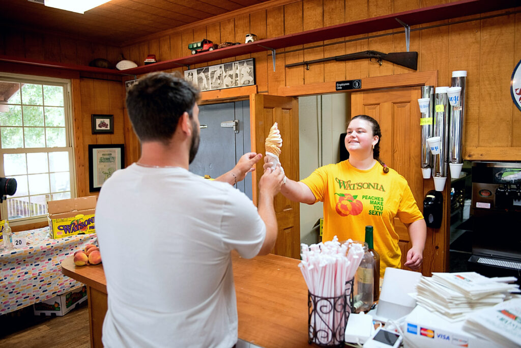employee at peaches n' such serves customer a peach ice cream waffle cone