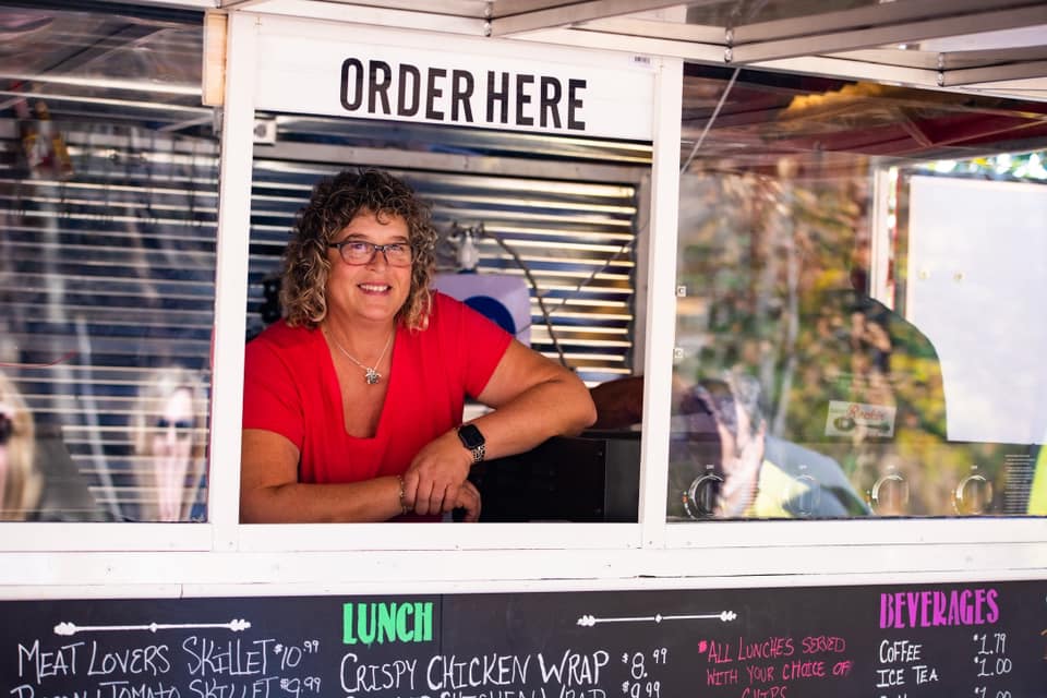 woman in red shirt smiling at pickup window at Sarah's Rockin' Kitchen food truck