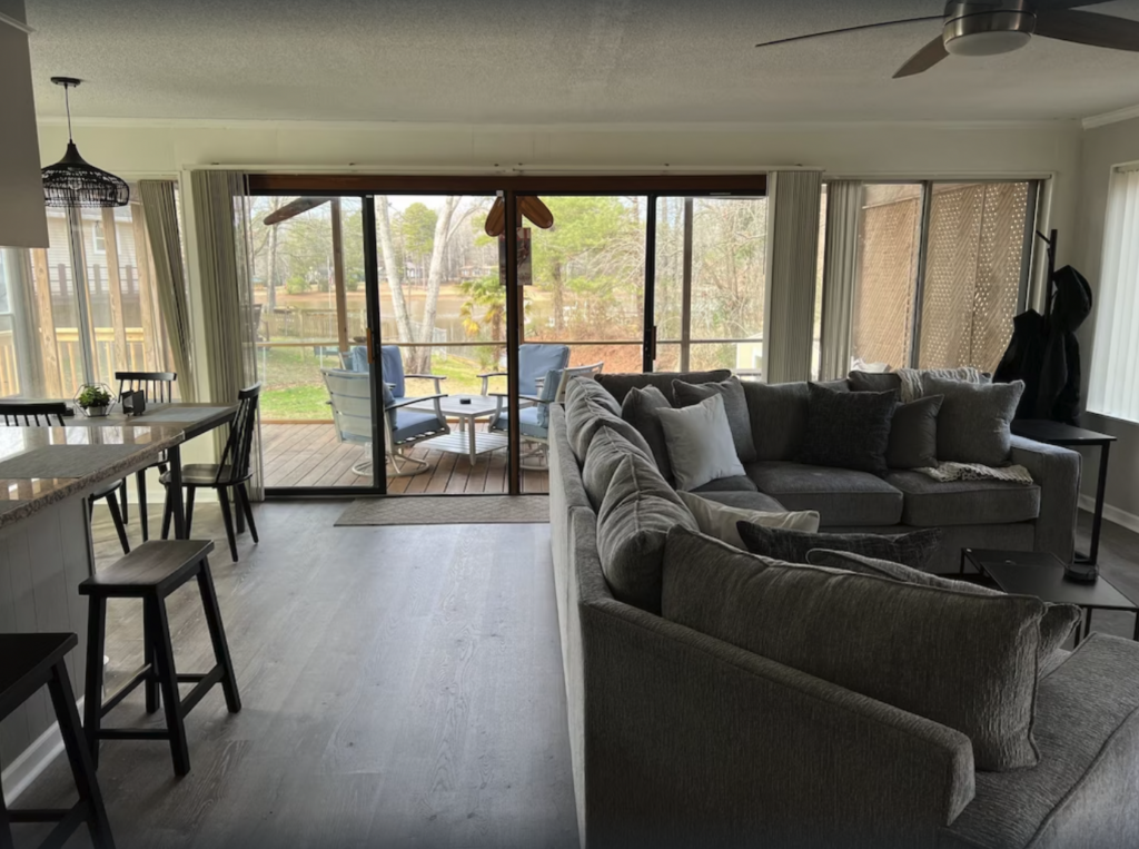view of great room with large gray couch and kitchen with bar seating and view of covered porch and water
