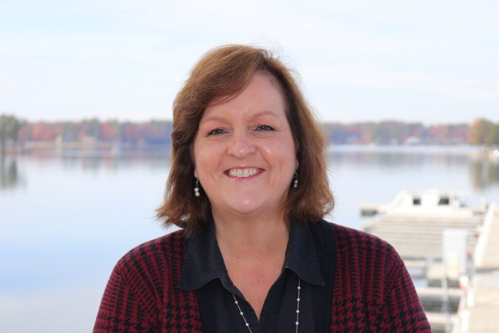 woman with shoulder length brown hair wearing a dark red blouse. Lake Murray is in the background