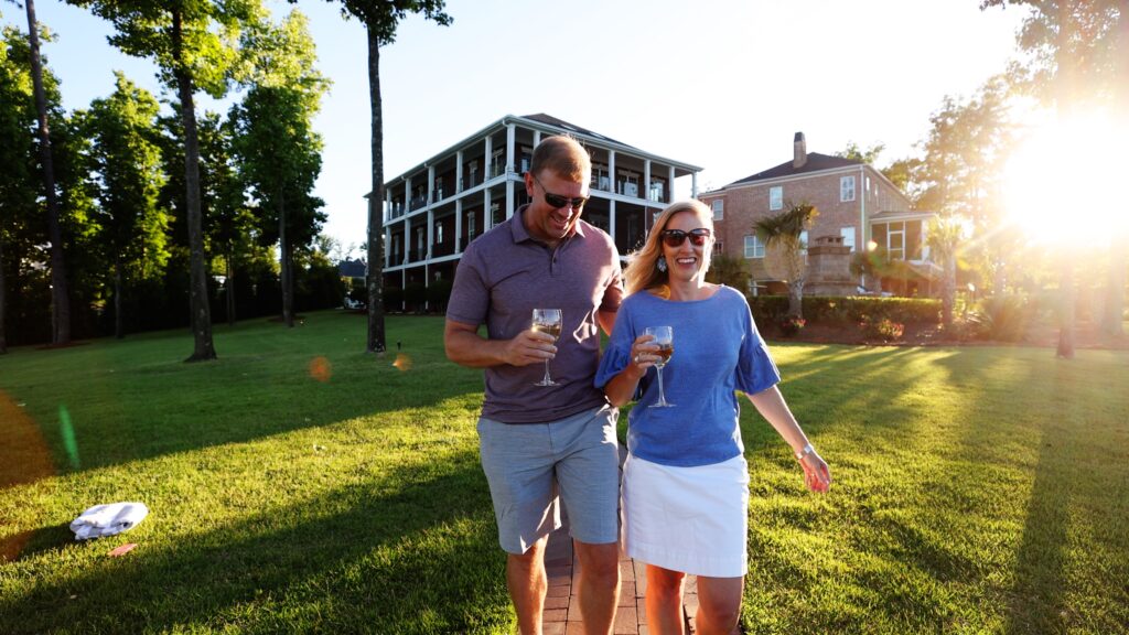 Man and woman walking holding glasses of wine with clubhouse in the background
