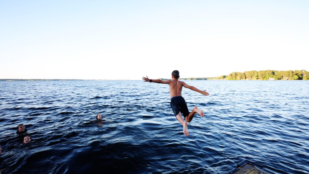 Young boy jumping in to the lake with arms wide open