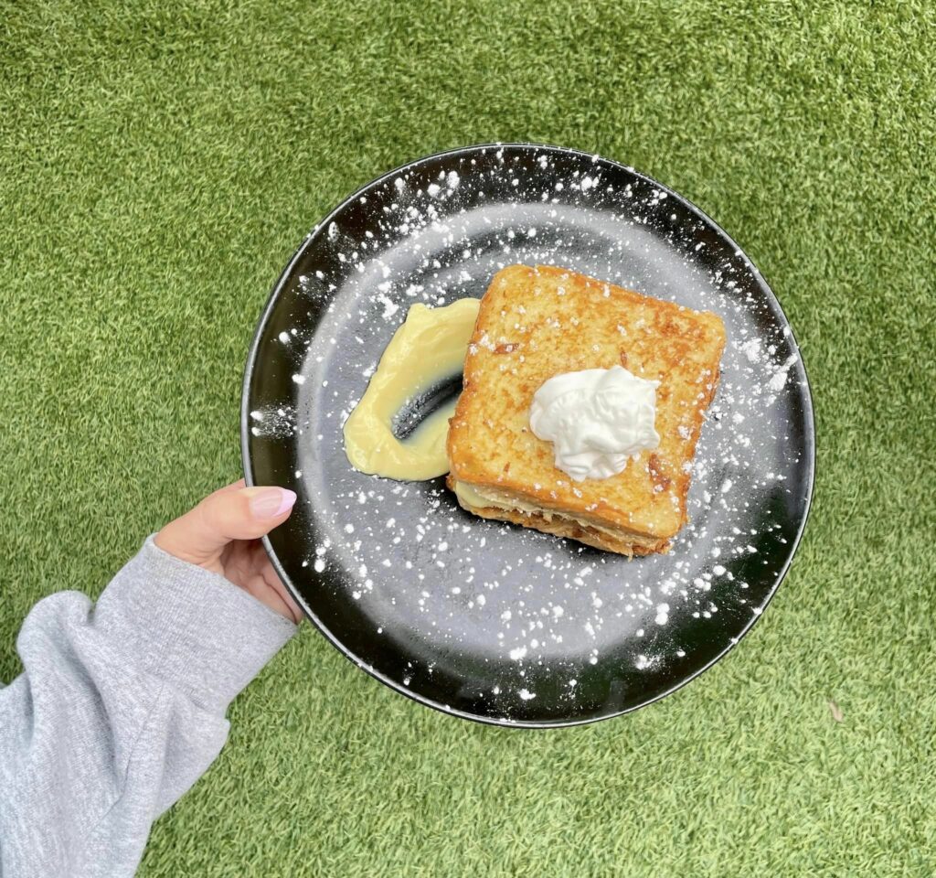 A delicious french toast with custard on a speckled black plate with a green grass turf background.