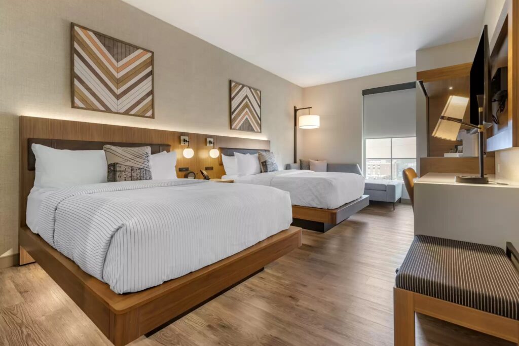 A beautiful double bedroom in the Cambria Hotel Columbia Downtown The Vista, with hardwood floors and white comforters.