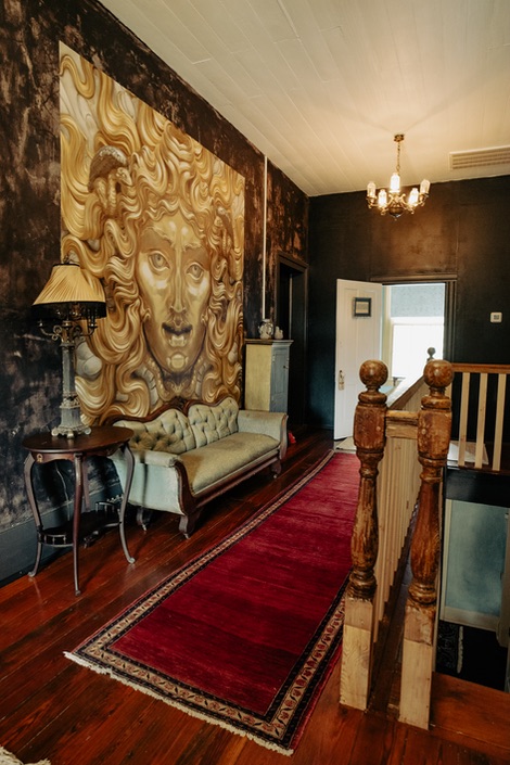 A beautiful golden face mural in the hallway lined with red velvet carpet and a mint green vintage couch upstairs at the gilded bat